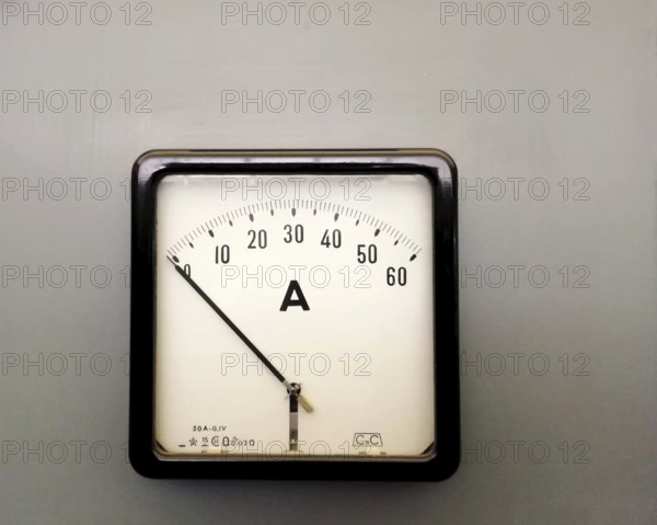 A large square industrial ammeter with an analogue dial with numbers with standard electrical symbols on a white dial on a grey background