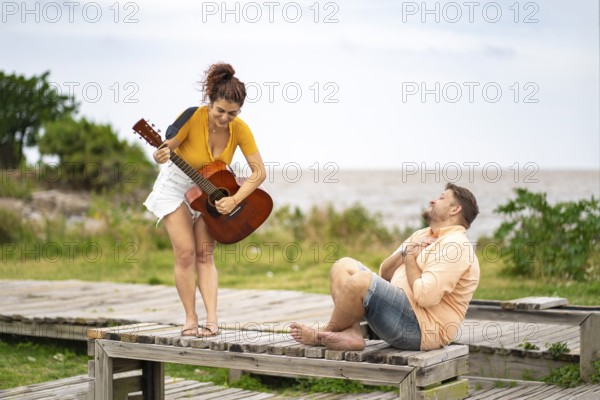 Man touches his chest in emotion as he listens to his girlfriend play guitar