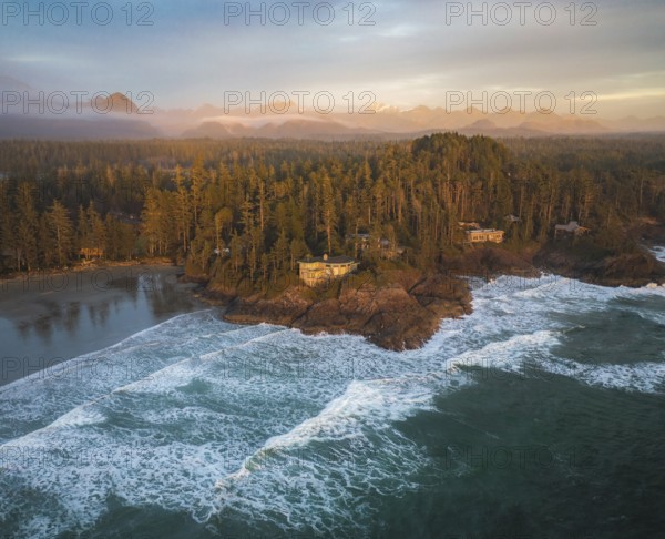 Aerial view of ocean waves crashing against a forested coastal island at sunset, with warm light illuminating the scene, Panorama shot, Tofino, BC, Canada, North America