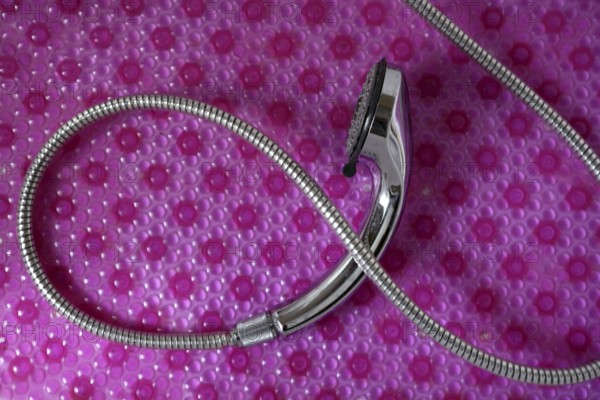 Bathroom chrome shower head with silver hose over pink background