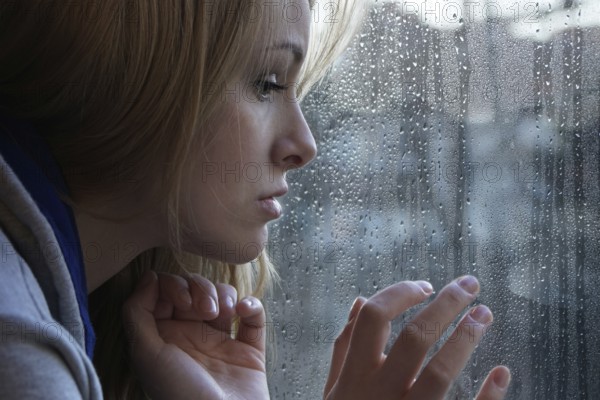 sad young woman looking through window on rainy day. depression concept