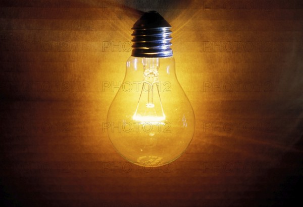Closeup of an old burning light bulb, switched on, a carton as background is illuminated, lit with a warm yellow and orange light