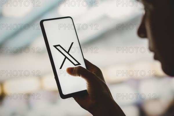 In this photo illustration, a silhouetted woman holds a smartphone with the Twitter (X) new logo displayed on the screen