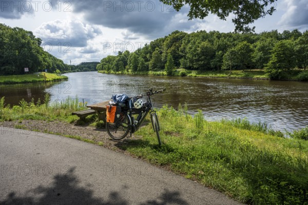A bicycle stands on a cycle path next to a peaceful river in nature, cycle tour along the Ems and Emsaltarm-Roheide