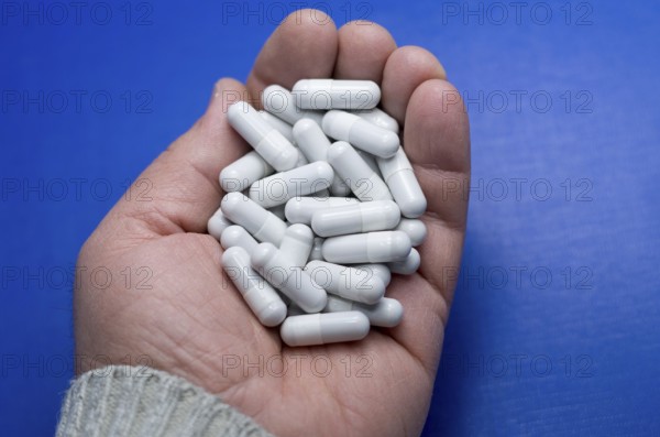 Large white pills fell from a large white bottle. Concept of drugs. Life without drugs and dependence on capsules of antibiotic, medicine, amphetamines, drugs and drugs. A male hand throws antibiotic capsules against a blue background. Bulgaria