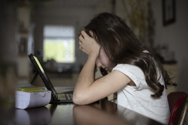 Girl, 10 years old, sits at the table with a tablet and learns