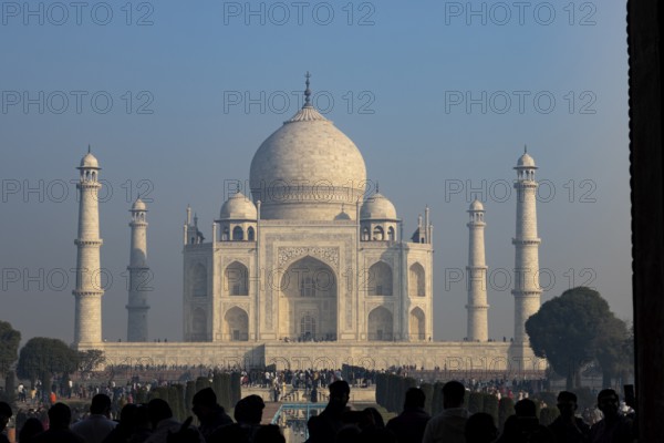 Taj Mahal, the mausoleum built for Mumtaz Mahal by her husband, the Mughal emperor, Shah Jahan. Wonder of the World, a UNESCO World Heritage Site, famous landmark and tourist attraction. View from the gateway with visitors watching and photographing. Winter morning light, clear blue sky. Agra, Uttar Pradesh, India, Asia