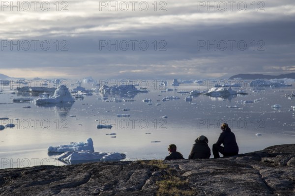 Rodebay, Greenland, July 09, 2018: A group of people sitting and looking at icebergs. Rodebay, also known as Oqaatsut is a fishing settlement north of Ilulissat, North America