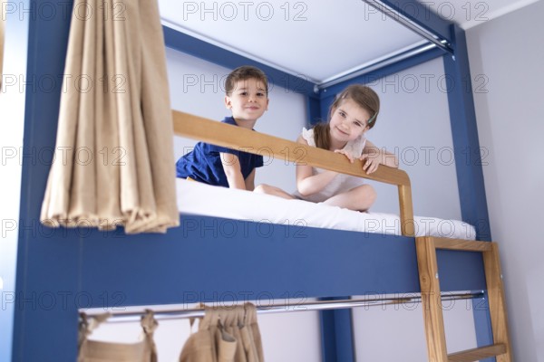 Caucasian little sibling are sitting on the bunk bed and looking to camera with big smile. Concept of love, relation, bonding friendship of brother and sister in family life