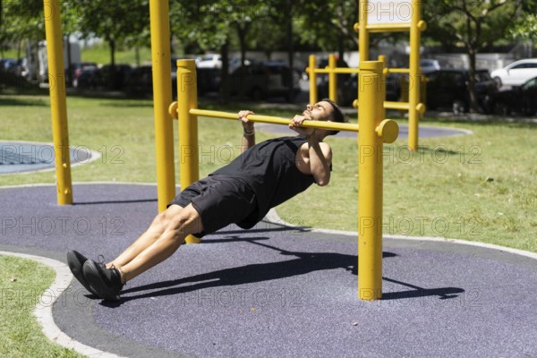 Young man performing inverted rows on outdoor bars.