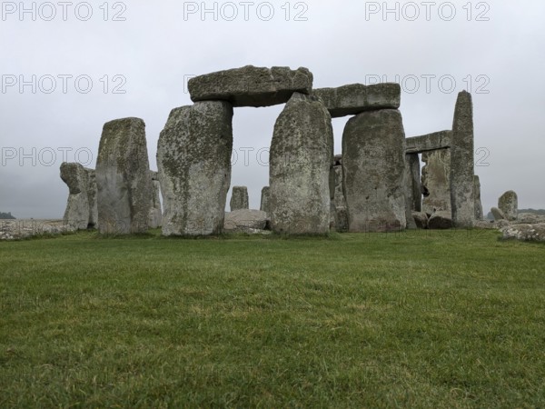 Close-up of Stonehenge with green grass and cloudy sky, emphasizing its ancient and historical nature. Salisbury, England, United Kingdom, Europe