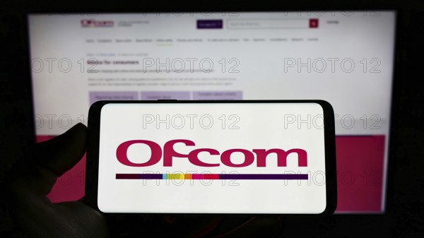 Stuttgart, Germany, 06-04-2022: Person holding cellphone with logo of British authority Office of Communications (Ofcom) on screen in front of webpage. Focus on phone display, Europe