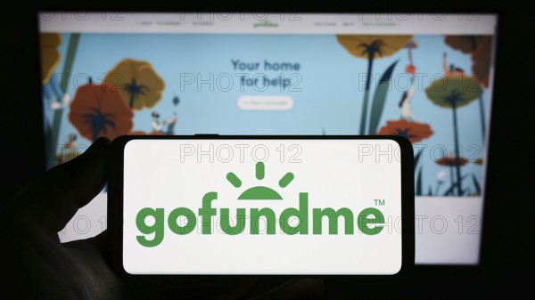 Stuttgart, Germany, 01-12-2023: Person holding smartphone with logo of crowdfunding platform company GoFundMe on screen in front of website. Focus on phone display, Europe