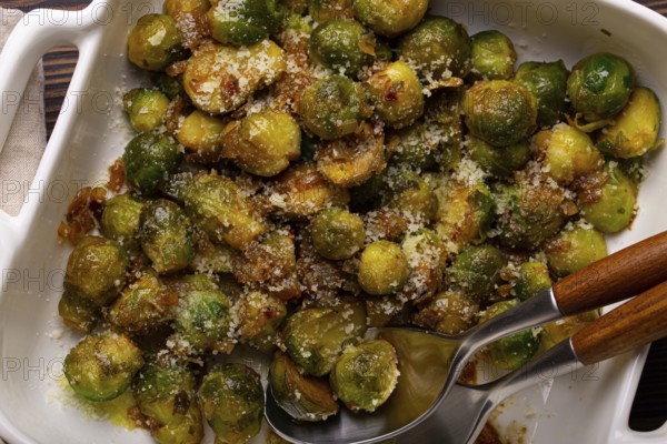 Healthy vegetarian dish roasted brussels sprouts with butter and parmesan cheese in white ceramic casserole top view on dark rustic wooden table from above, vegan food