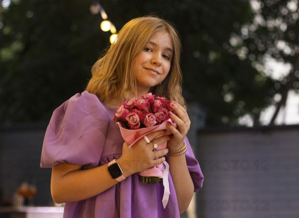 Cute teen girl with rose flowers. Child playing in summer garden. Kids gardening. Children play outdoors. Blond female with flower bouquet for birthday or mother s day