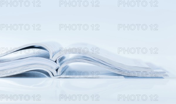 Stack of open magazines in blue tone on white background with copy space