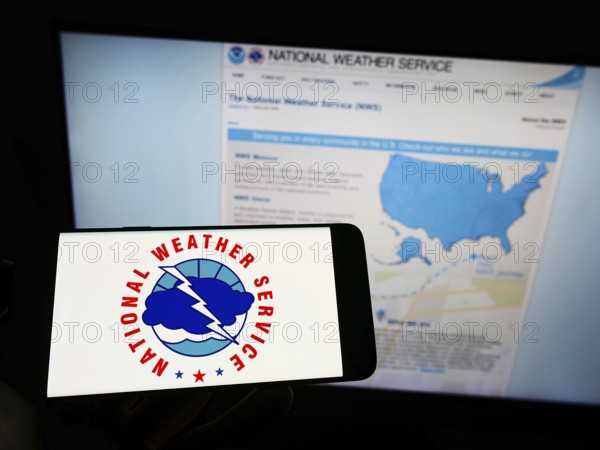 Stuttgart, Germany, 09-30-2022: Person holding cellphone with logo of US agency National Weather Service (NWS) on screen in front of webpage. Focus on phone display, Europe
