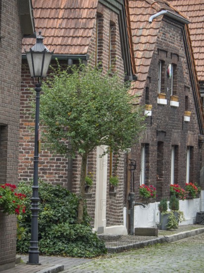 A quiet alley with brick houses, a alleyway lamp and a tree, flowers hanging from the windows, Hünxe, Lower Rhine, Germany, Europe