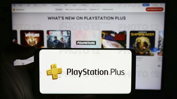 Stuttgart, Germany, 02-14-2024: Person holding cellphone with logo of subscription service PlayStation Plus (PS Plus) in front of business webpage. Focus on phone display, Europe