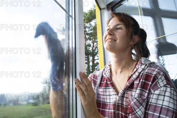 Woman manually washes the window of the house with a rag with spray cleaner and mop inside the interior with white curtains. Restoring order and cleanliness in the spring, cleaning servise