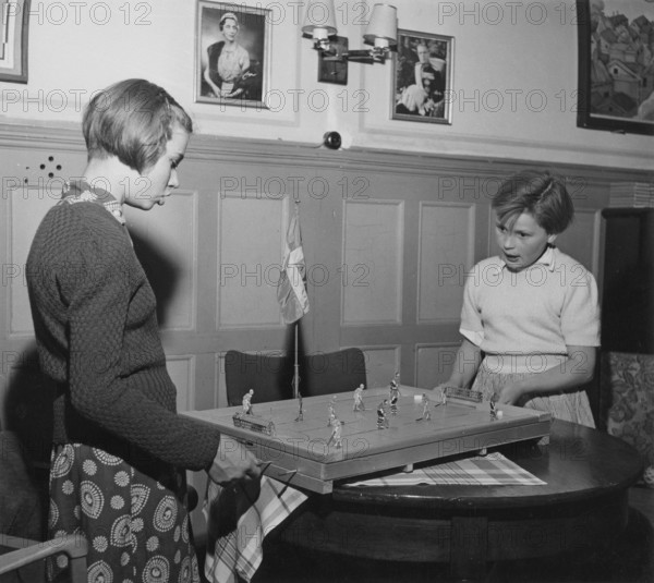 In the 1950s. Two girls are playing the Ice Hockey game Puck. Manufactured by Swedish company Aristospel. At this time patented and alone on the market to sell the game. The players maneuver the figures on the board by moving and twisting them around and like real hockeyplayers move the puck around to try to score a goal. 1950s