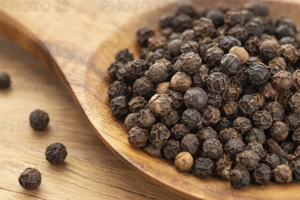 Black pepper (Piper nigrum) or pepercorn on wooden spoon. Cooking Spices.