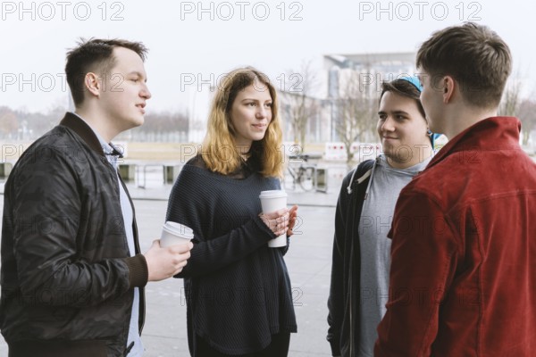 group of teenage friends having a conversation while standing together on city street holding coffee cups