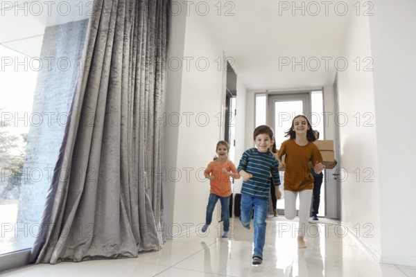 Happy family running in hall. Funny kids jumping with carton box, parents laughing, play with children have fun together move at new house. Mortgage loan and relocating concept