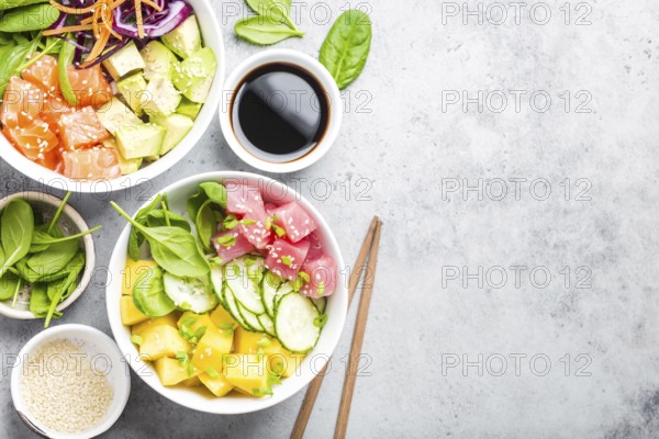Two assorted poke bowls with raw fish and vegetables, space for text. Top view, close up. Hawaiian dish, rustic stone background. Healthy clean eating concept. Poke with raw fish slices, copy space