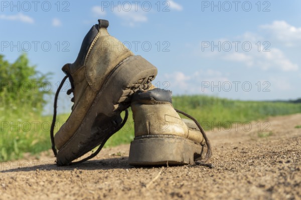 Pair of old worn leather hiking boots an a gravel path or road balanced on top of one another in a close up view
