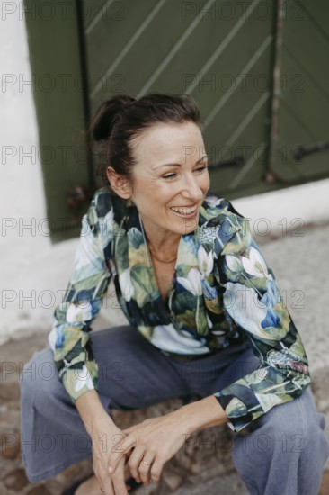 Smiling, dark-haired woman, 40+, sitting on a staircase