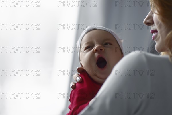 Mother holding cute newborn baby girl in her arms. Sleepy baby yawning