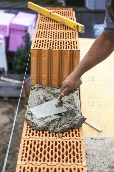Anonymous construction worker on a building site erecting a brick wall. Brick wall of a solid house. Symbolic image for illegal labour and bungling