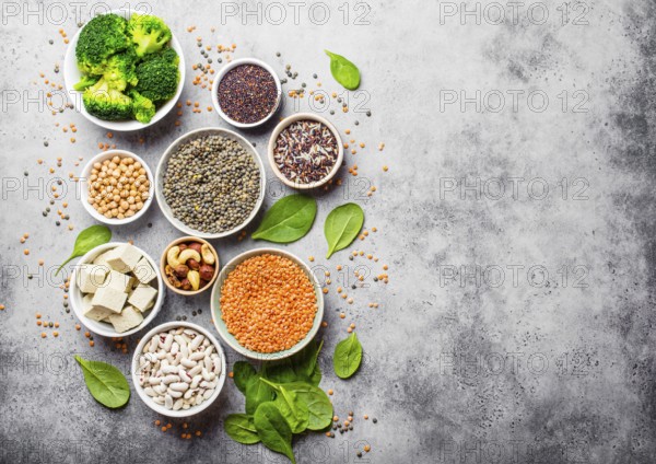Top view of different vegan protein sources with space for text: beans, lentils, quinoa, tofu, vegetables, nuts, chickpeas, rice, stone background. Healthy balanced vegetarian nutrition for vegans
