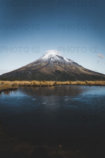 A snow-capped mountain reflected in a still lake under a clear blue sky, Mount Taranaki, New Zealand, Oceania
