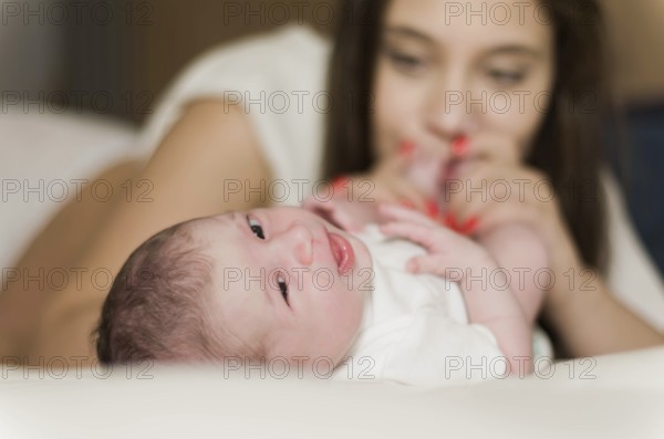 Young caring mother playing with her newborn son on the bed, happy moments of motherhood
