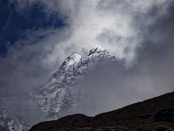 Two brightly lit snowy peaks peeking out of the clouds behind a dark ridge, Annapurna region, Nepal, Asia