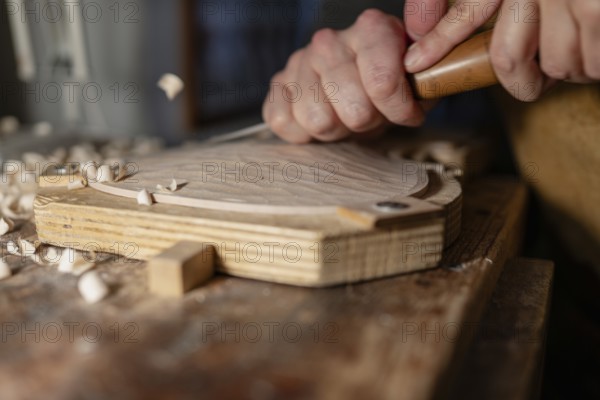 Luthier using gouge and mallet, shaping wood for a violin in his workshop, surrounded by wood shavings
