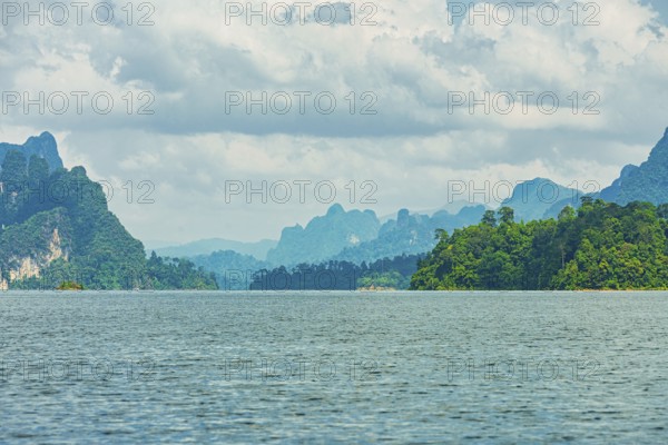 Distant mountains on a cloudy horizon overlook a vast lake, offering a calm natural scene, Cheow Lan Lake, Khao Sok National Park, Thailand, National Park, Khao Sok lake, water, mountains, green, Asia