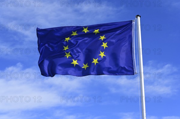 The flag of the EU European Union flutters in the wind against a blue cloudless sky