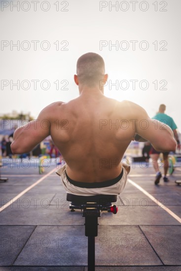 A man exercises outdoors in the sunlight, concentrating on strengthening his back muscles on a rowing machine, Barcelona, Spain, Europe