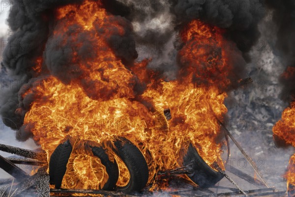 Burning automobile tires, strong flame of red fire and clouds of black smoke in sky. Selective focus, blur from strong fire