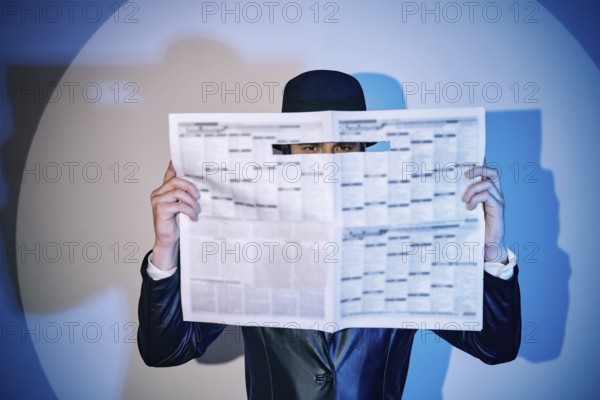 Man hiding watches through the newspaper in the spotlight on studio background. noir film style. Private detective, investigation, secret, detective, espionage concept