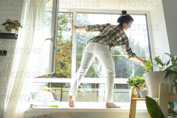 Woman manually washes the window of the house with a rag with spray cleaner and mop inside the interior with white curtains. Restoring order and cleanliness in the spring, cleaning servise