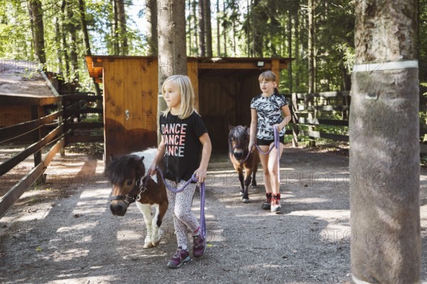 Children walking with ponies, small horses, holding them for a leash. Cute mini horses walking with children on the ranch
