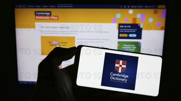 Stuttgart, Germany, 07-11-2023: Person holding cellphone with logo of Cambridge Dictionary on screen in front of webpage. Focus on phone display, Europe