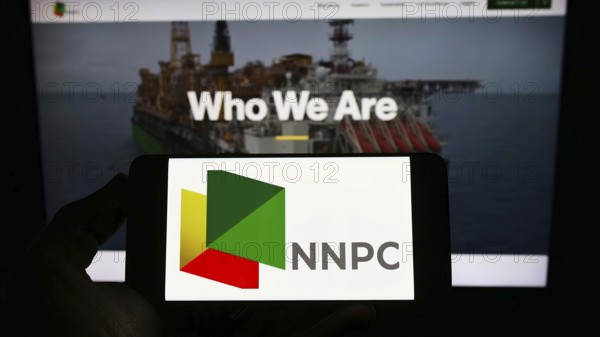 Stuttgart, Germany, 10-03-2022: Person holding smartphone with logo of Nigerian National Petroleum Company Limited (NNPC) on screen in front of web page. Focus on phone display, Europe