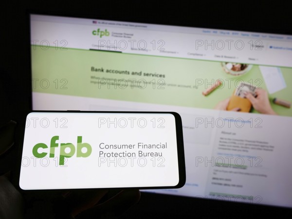 Stuttgart, Germany, 09-18-2022: Person holding mobile phone with logo of US Consumer Financial Protection Bureau (CFPB) on screen in front of web page. Focus on phone display, Europe