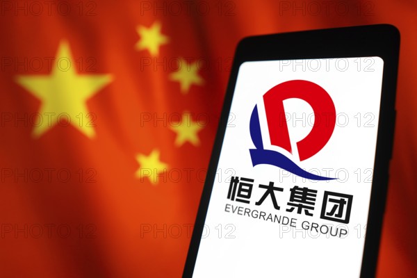 In this photo illustration, the Evergrande Real Estate Group logo is displayed on a smartphone screen and in the background, the flag of China