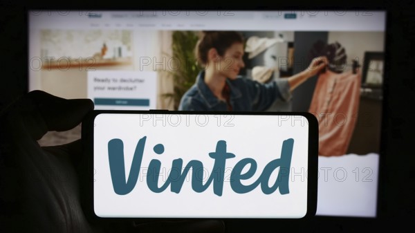 Stuttgart, Germany, 03-17-2024: Person holding cellphone with logo of online secondhand marketplace company Vinted in front of business webpage. Focus on phone display, Europe